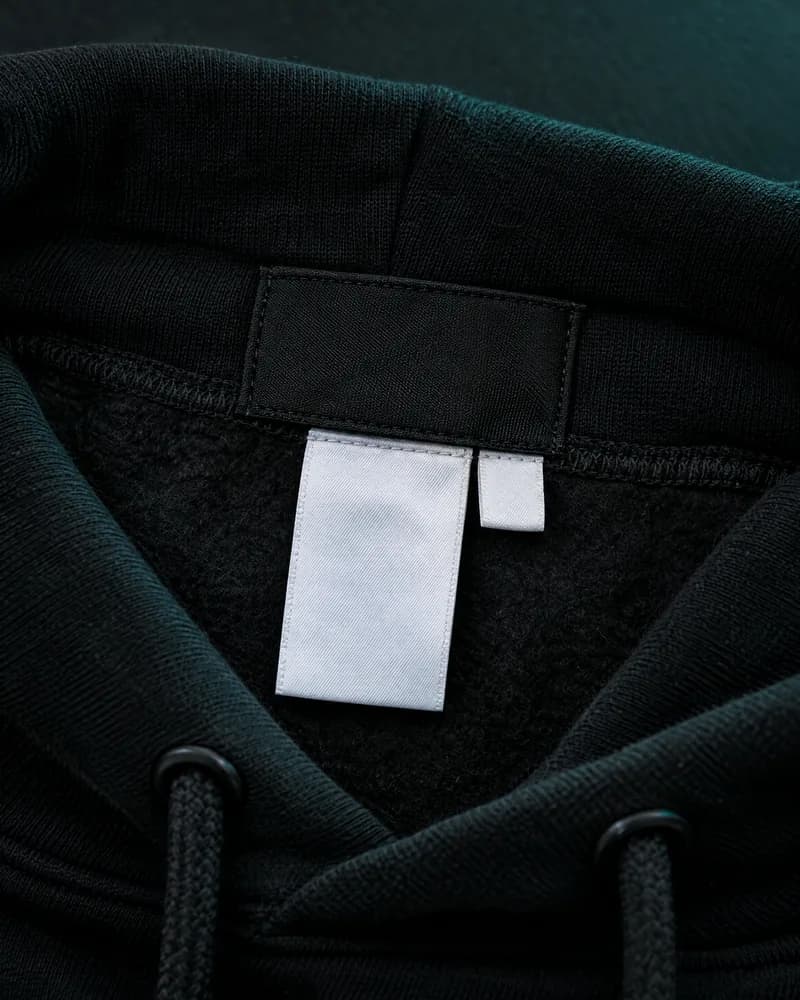 Illustration of the inside of a black hoodie collar with a blank neck label, a blank care label and a small blank tag