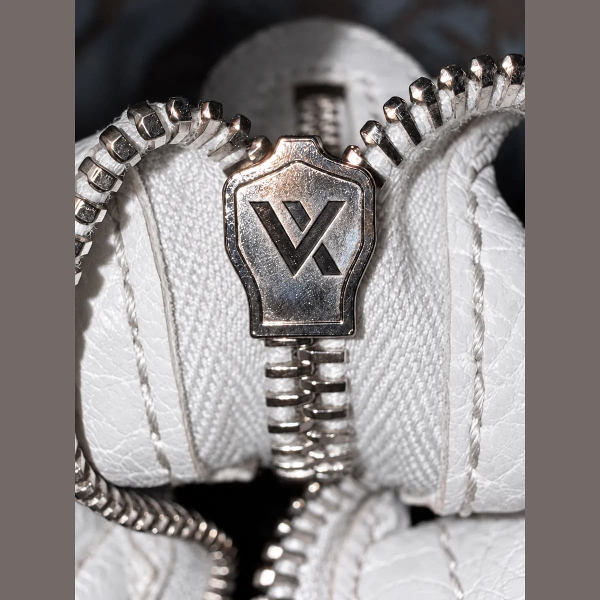 Sample photo 13, Zipper Bottom: the bottom of a zipper on white leather, with a pull that carries the Vereev logo